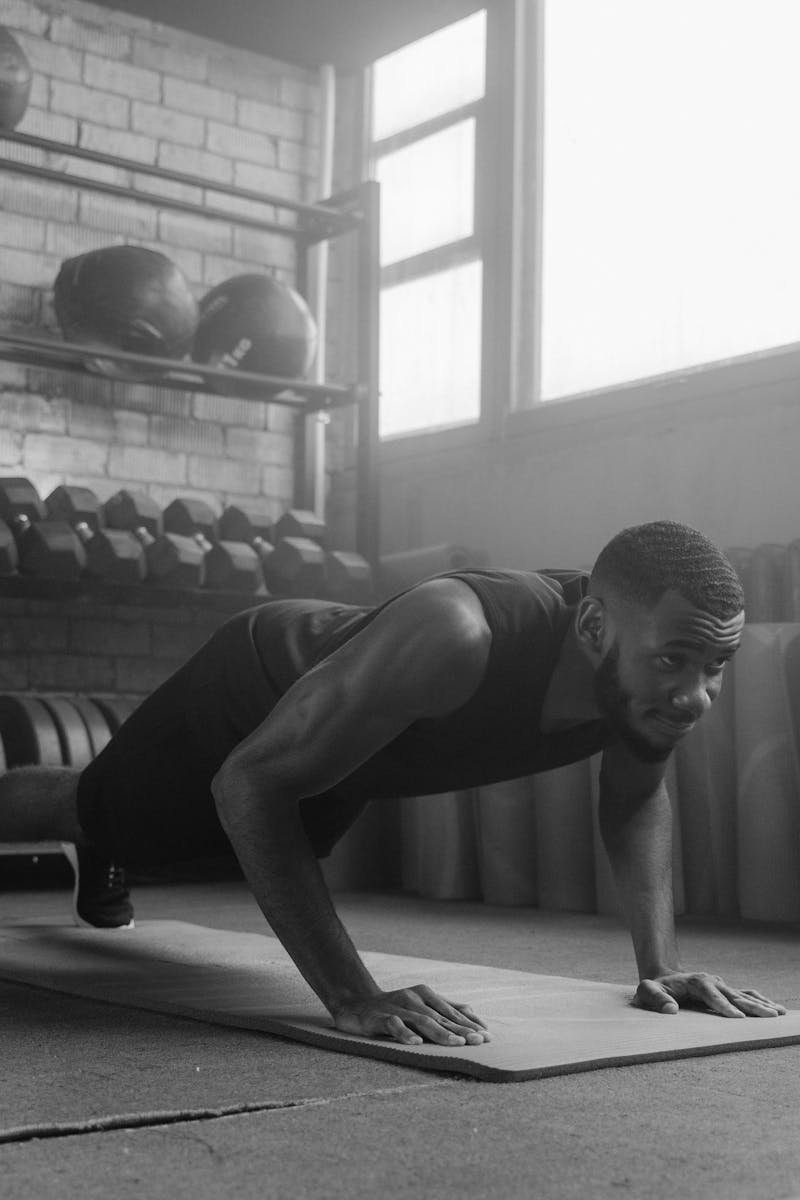 Monochrome image of a man doing push-ups on a mat in a gym setting.